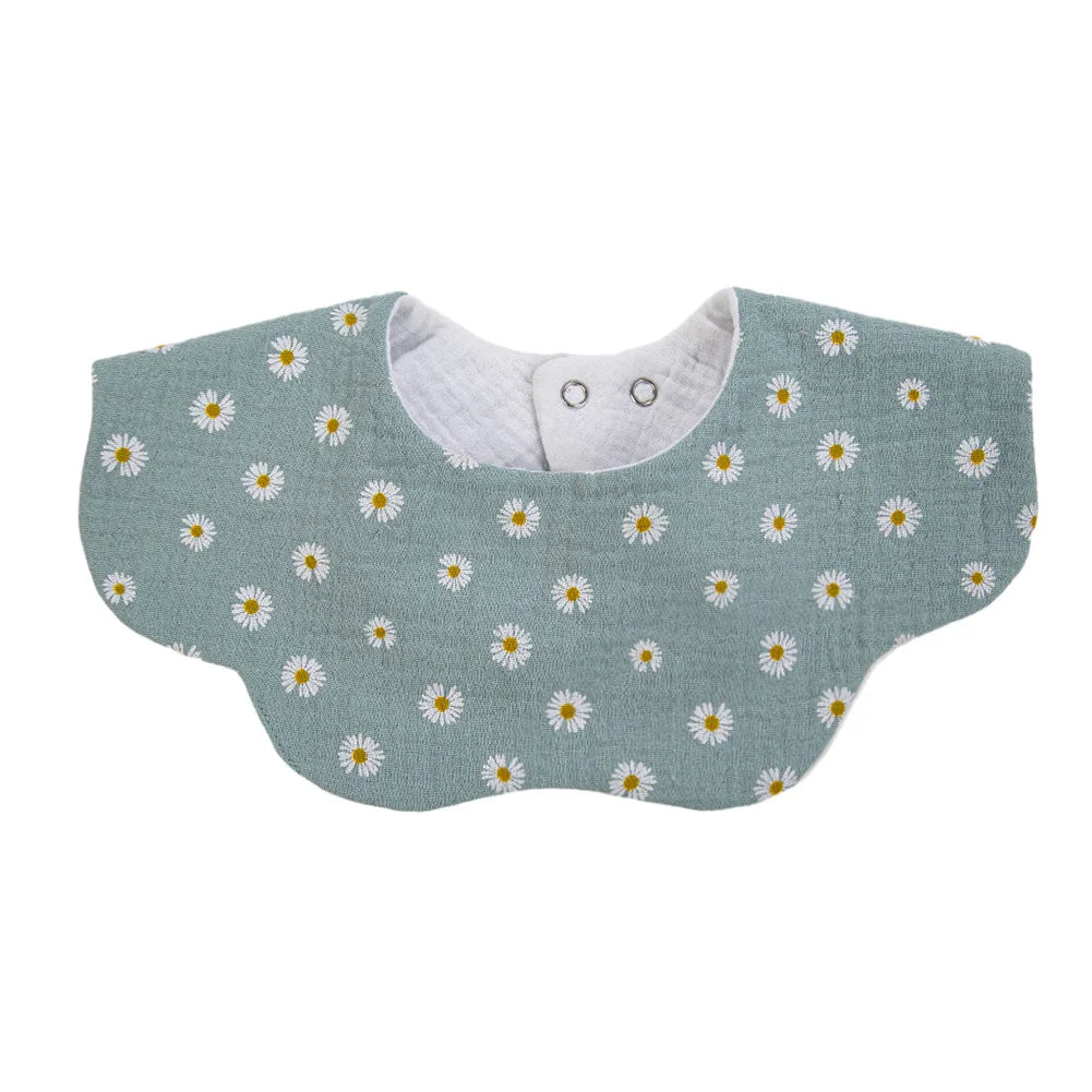 A light sage green muslin cotton baby bib with a white daisy pattern and an adjustable snap closure.