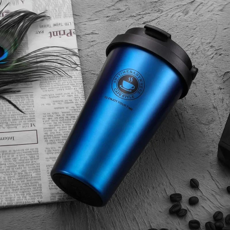 Mattblaue doppelwandige Thermos-Tasse auf einer strukturierten Oberfläche neben gedrucktem Papier.