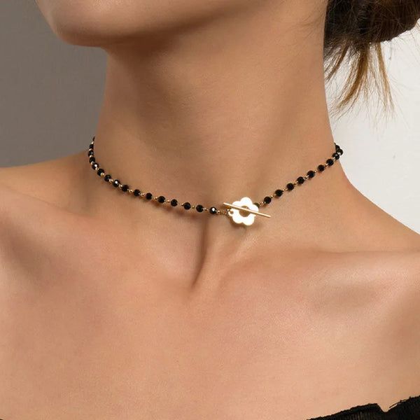 Collier de perles noires avec pendentif carré géométrique blanc, porté autour du cou.