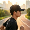 A young man wearing a black short brim quick-dry mesh baseball cap is running outdoors on a paved road at sunset.