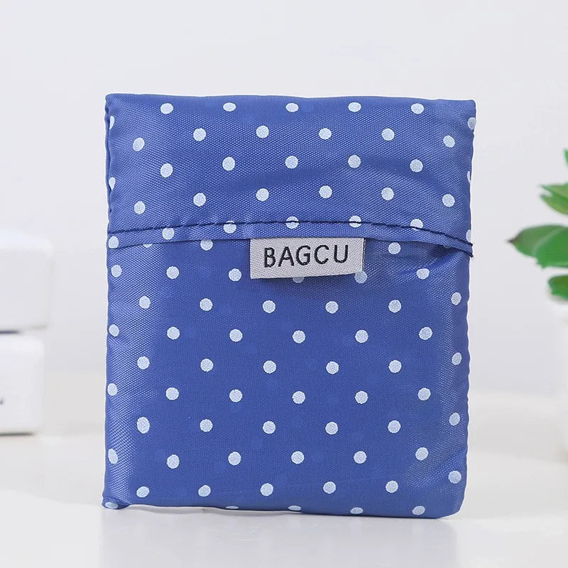A folded blue fabric shopping bag with white polka dots resting on a white surface.