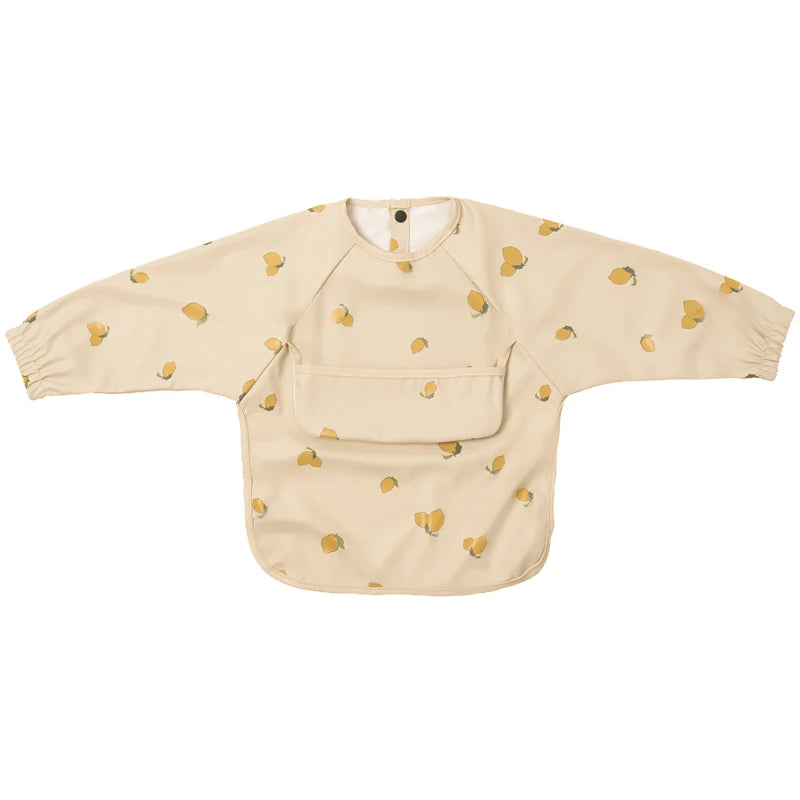 A beige waterproof long-sleeve smock for toddlers with a pocket and small yellow fruit print.