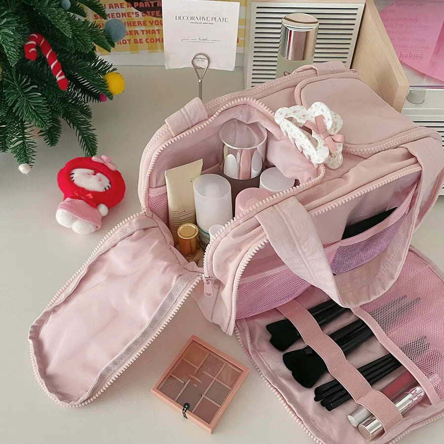 A pink cosmetic travel organizer bag with multiple compartments and a matching pink cosmetic case is shown on a light surface