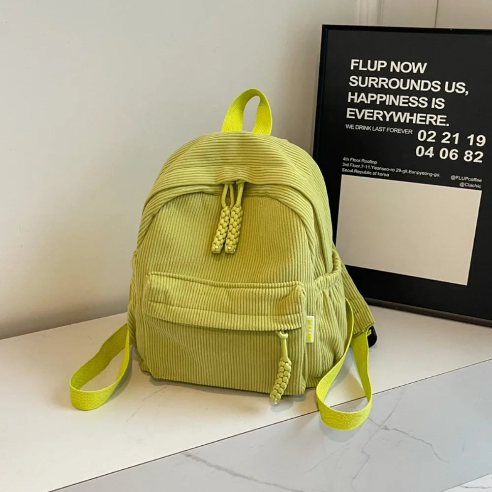 A lime green corduroy casual backpack is displayed on a white surface next to a framed sign.