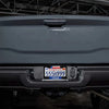 Close-up of a gray vehicle's rear, featuring a Texas license plate frame with the state flag design.