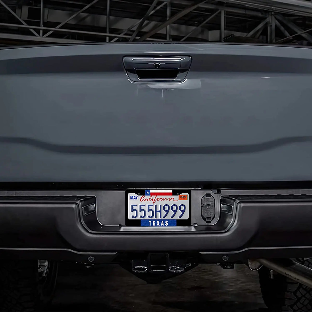Close-up of a gray vehicle's rear, featuring a Texas license plate frame with the state flag design.