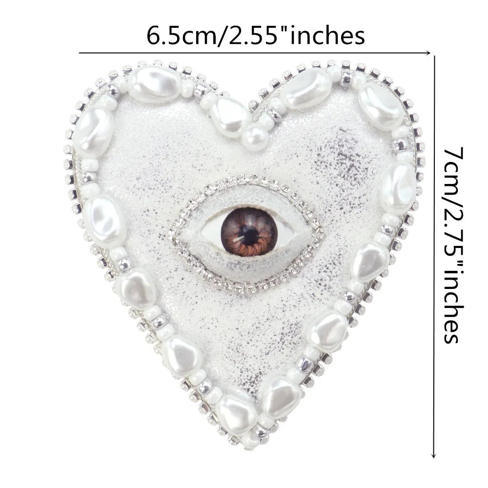 A heart-shaped patch featuring a sparkling silver background and a central realistic eye design surrounded by pearl beads.
