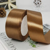 A roll of luxurious satin ribbon in a golden brown color shown next to a piece of paper.