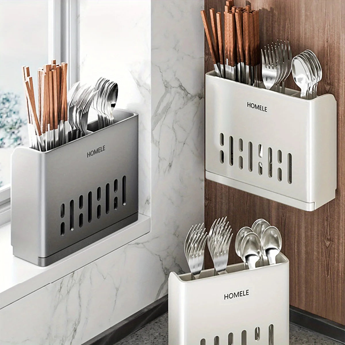 A set of stainless steel cutlery is stored in a modern, rectangular organizer box on a marble countertop.