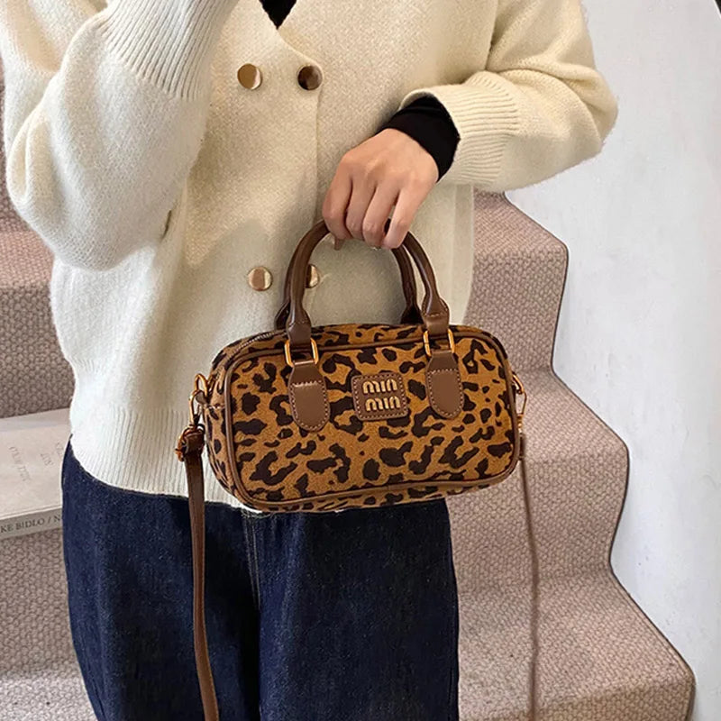 A woman holds a brown retro leopard print hobo satchel bag against a light beige sweater and dark jeans.
