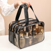 A transparent PVC travel toiletry bag with black straps is held by a hand, showing various bottles inside.