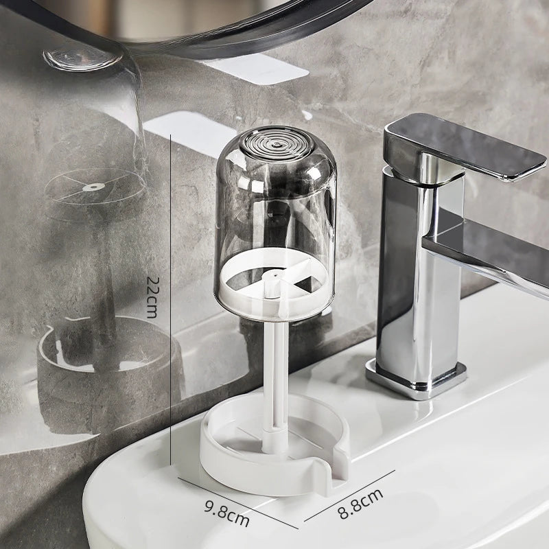 A modern chrome toothbrush holder with a dust cover and drainage mechanism mounted on a white bathroom sink.