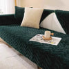 A dark green velvet sofa cushion mat with a white pillow and an open magazine resting on it.