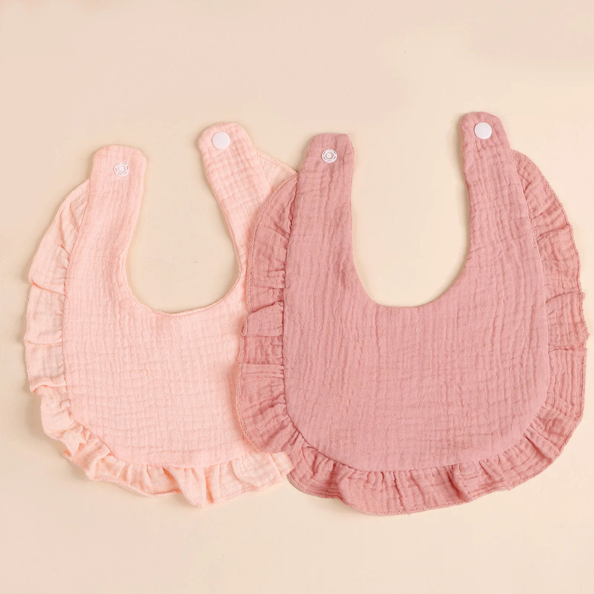 A set of three pink soft cotton ruffle bibs for babies displayed on a light background.