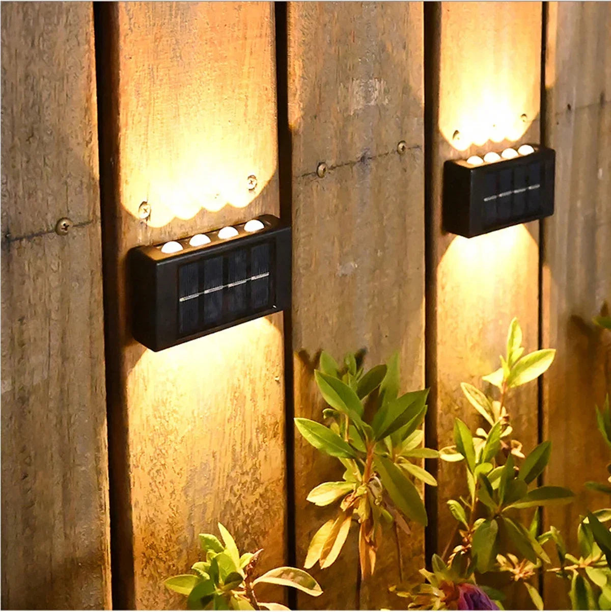 A solar powered wall light illuminates a wooden panel, casting a warm glow on surrounding foliage.