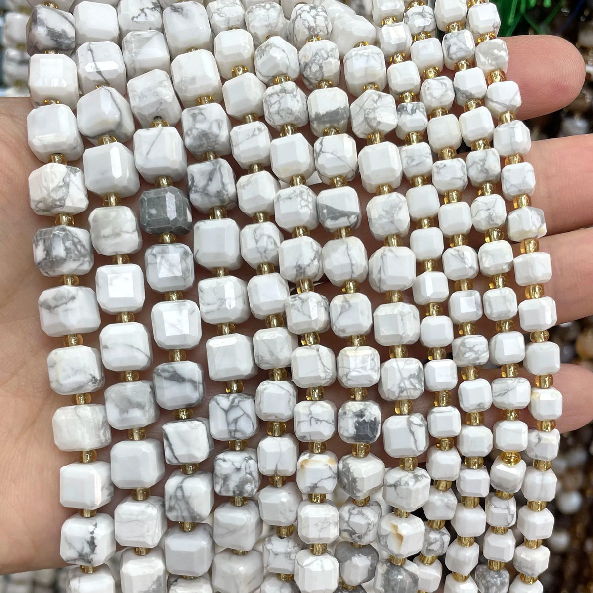 A close-up of natural stone square faceted beads in white and gray marble colors being held in a hand.