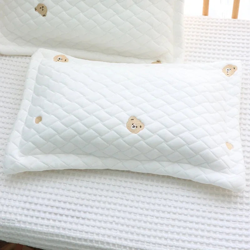 A white quilted baby pillow with a removable ice silk cover resting on a white textured surface.