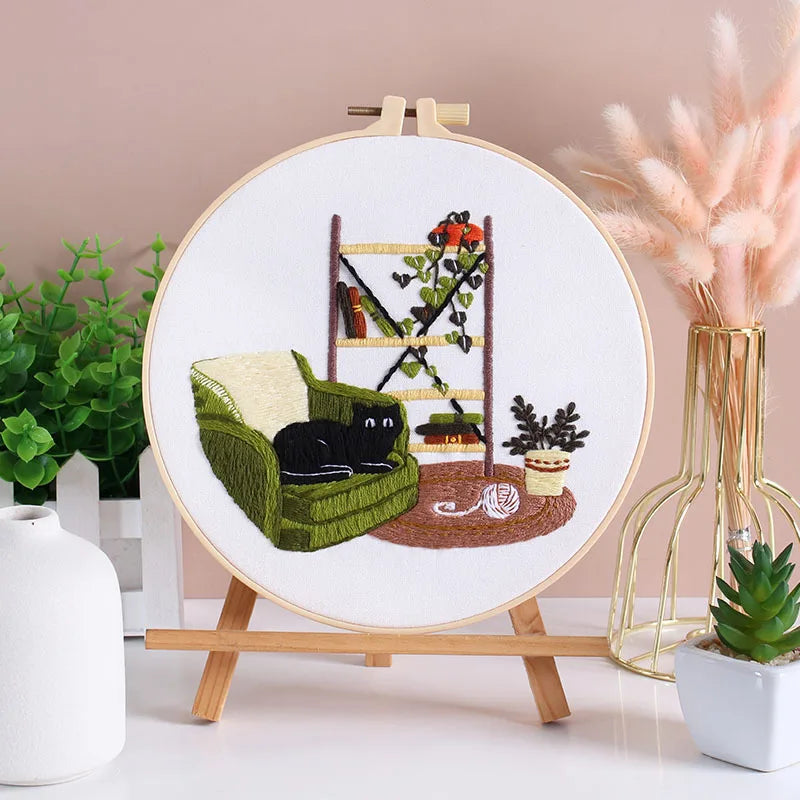 Embroidery kit featuring pre-printed floral and cat designs on fabric displayed on a wooden easel.