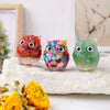 Handcrafted crystal owl figurine in vibrant colors with a natural crushed stone finish displayed on a white rock.