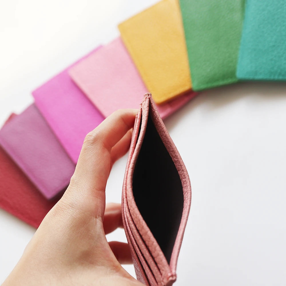 A hand holds a folded genuine leather slim card holder wallet displaying various pastel colors.
