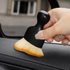 A hand holds a black and natural fiber curved detailing brush resting on a black car interior surface.