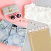 Kraft bubble mailers with self-seal adhesive placed next to sunglasses, a clutch, and a white garment on a pink background.