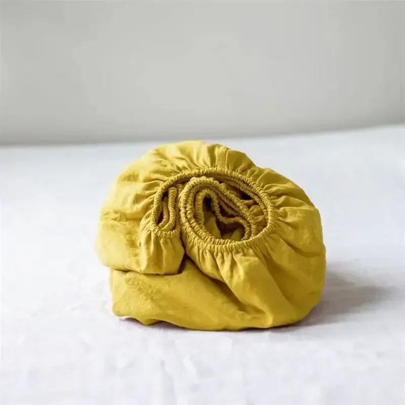 A rolled yellow linen fitted sheet with deep pockets resting on a white surface.