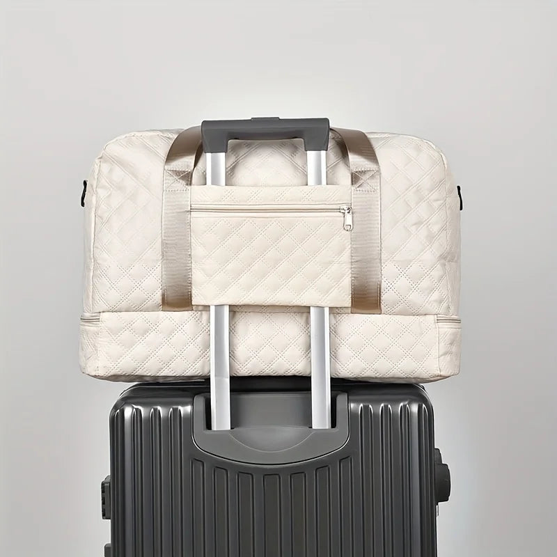 A beige lightweight nylon travel duffle bag with a silver handle resting on top of a gray suitcase.