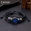 A black leather wrap bracelet featuring a glowing blue zodiac sign charm on a silver metal setting.