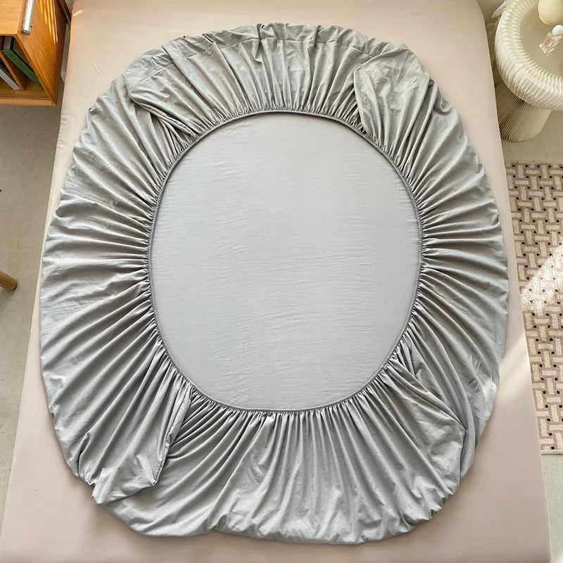 A light gray fitted sheet with gathered fabric folds is displayed on a surface.
