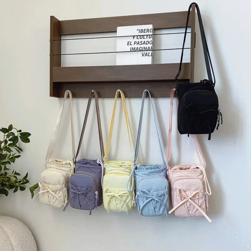 A collection of light-colored and pastel fabric crossbody bags hanging on a wooden shelf.