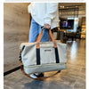 A beige travel duffle bag with black accents is being held by a person in a modern indoor setting.