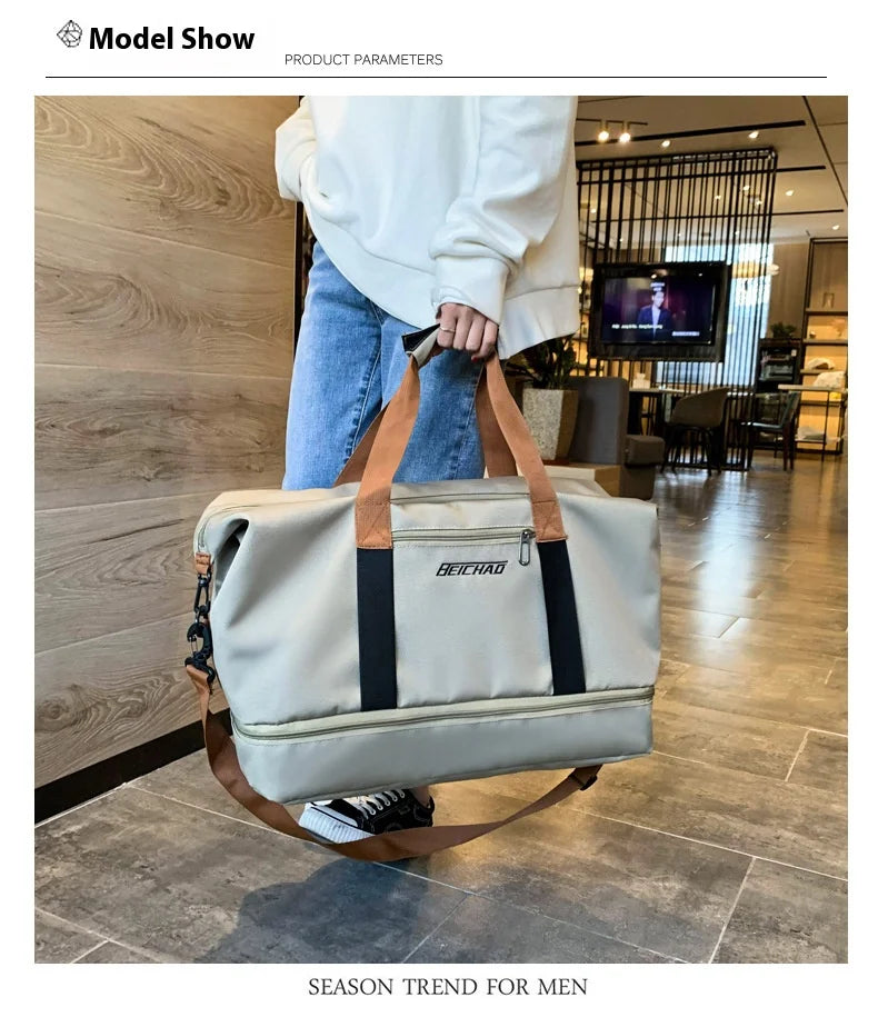 A beige travel duffle bag with black accents is being held by a person in a modern indoor setting.