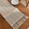 Beige boho table runner with tassels hand-woven farmhouse style placed on a wooden table.