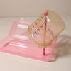 A pink silicone baby bottle cleaning set with a clear bottle and a brush is displayed on a pink tray.