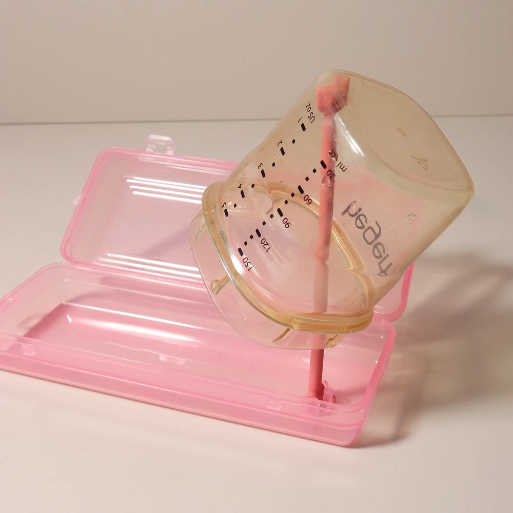 A pink silicone baby bottle cleaning set with a clear bottle and a brush is displayed on a pink tray.