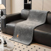 A gray quilted plush sofa cover with a non-slip backing draped over a dark leather sofa.