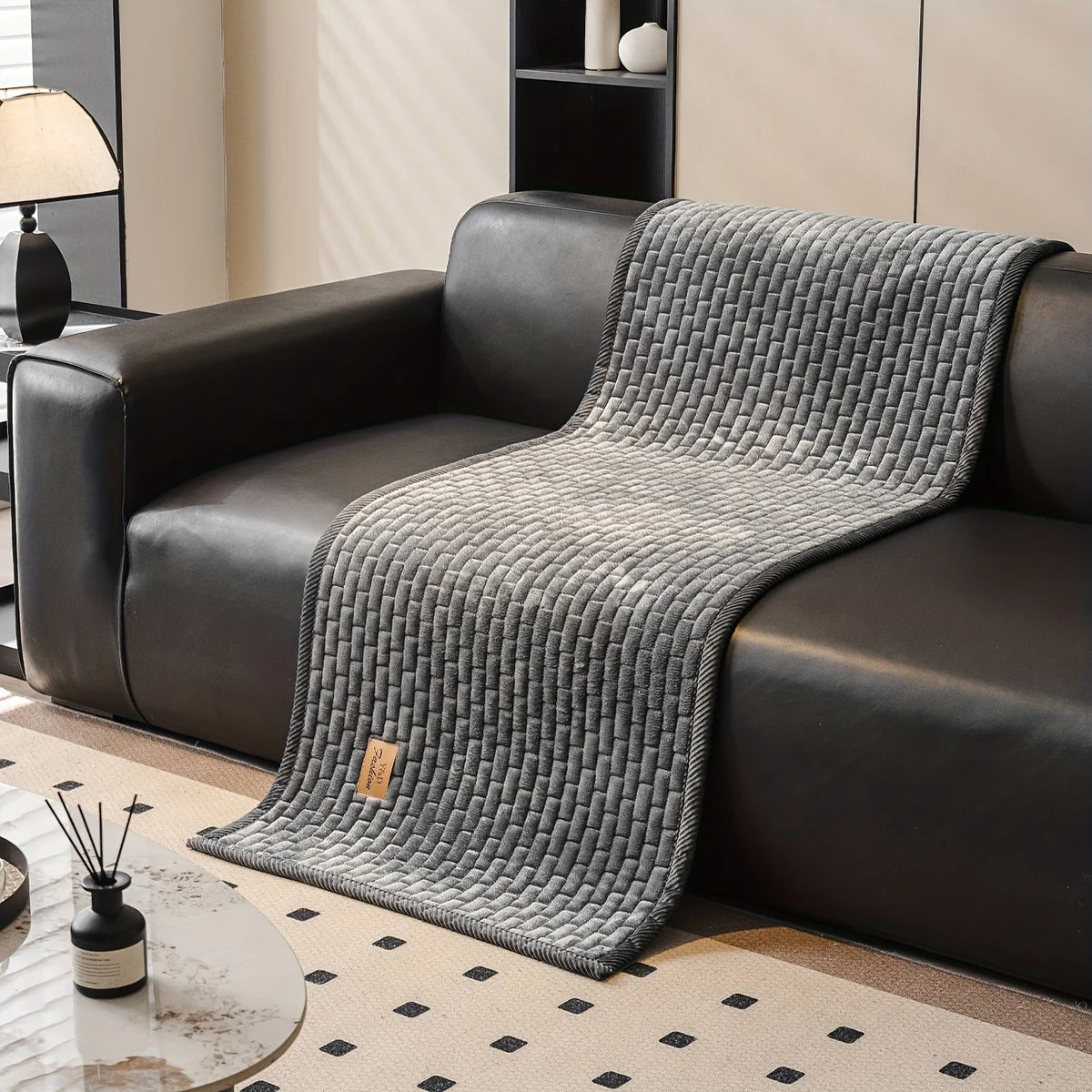 A gray quilted plush sofa cover with a non-slip backing draped over a dark leather sofa.