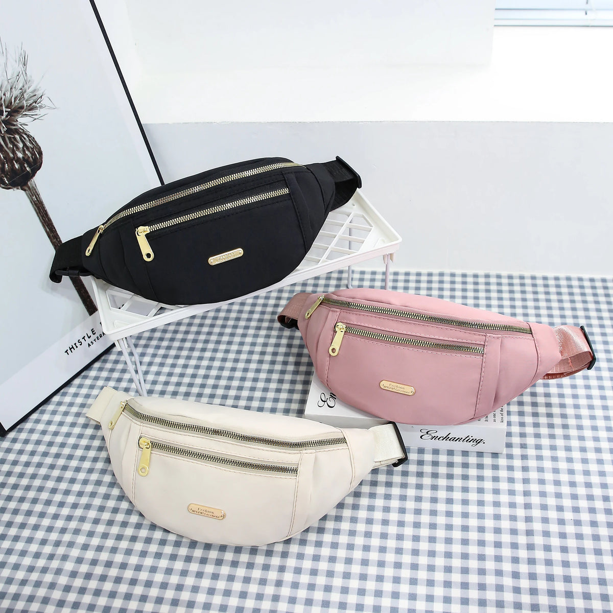 Drei Damen-Sport-Fanny Packs in Schwarz, Pink und Beige auf kariertem Untergrund.