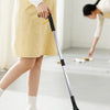 A person uses a foldable reacher grabber tool to pick up cleaning items on a floor.
