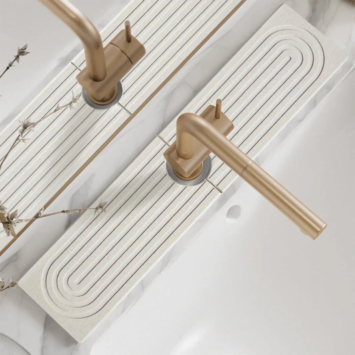 A brass faucet mat with concentric grooves is shown next to a white marble countertop.