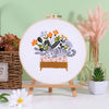 Embroidery starter kit featuring pre-printed floral and cat designs displayed on a wooden board.