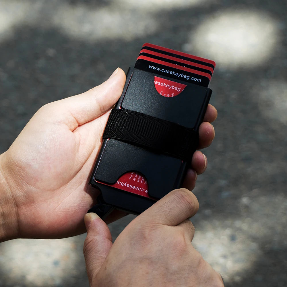 Eine Hand hält eine schwarze, schlanke RFID-blockierende Metalldosierkarte mit roten Akzenten.