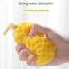 A hand is squeezing a yellow soft mesh bath sponge ball for baby, demonstrating strong water absorption.