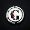 Silberner Briefhaken mit einem geschnitzten Initial G, umgeben von kleinen rosa und lila Blumen