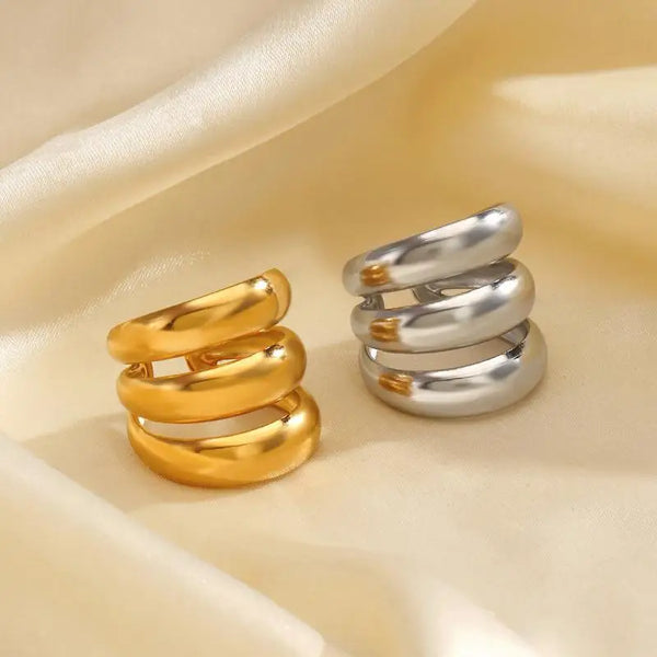 A pair of chunky multi-tone dome rings, one gold and one silver, displayed on a soft cream fabric.