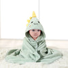 A baby wearing a light green hooded towel with a yellow cartoon design lying on a white surface.