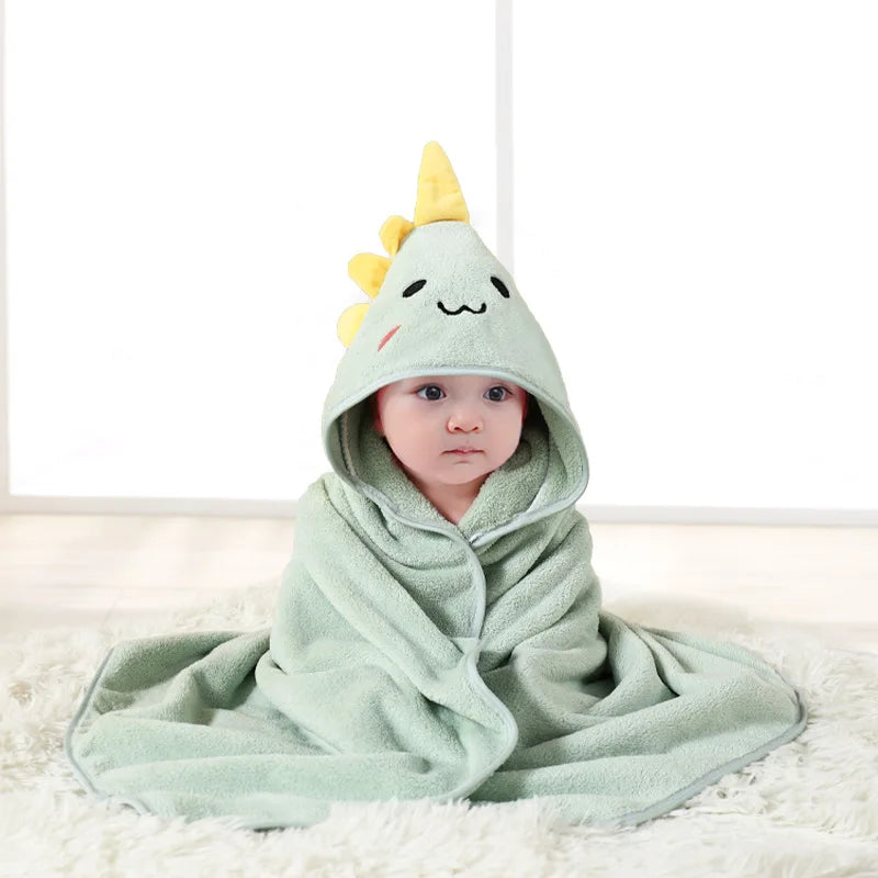 A baby wearing a light green hooded towel with a yellow cartoon design lying on a white surface.