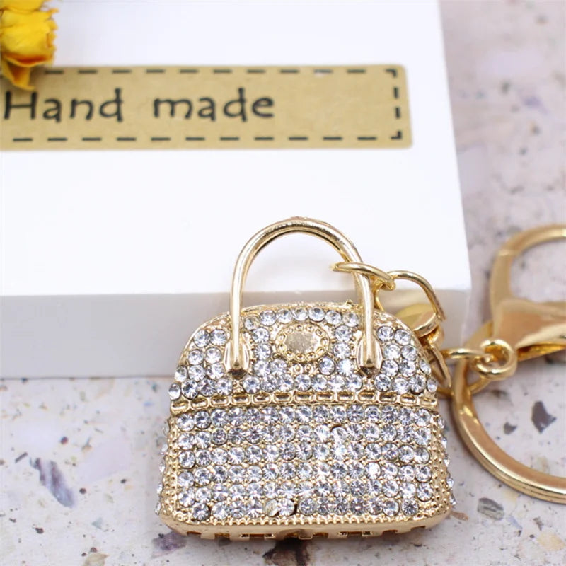 Gold crystal rhinestone handbag keychain with a textured surface resting on a white background.