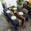 A dark blue geometric waterproof tablecloth set for a dining table with gold and white plates and a centerpiece.